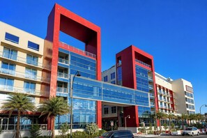 A multi-story hotel with a red and beige facade, large windows, and a pedestrian bridge.