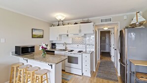 A modern kitchen with white cabinets, a granite countertop, a microwave, a coffee maker, and a refrigerator. - Oceanfront Sea Cabin on the Front Beach of Isle of Palms (Isle Of Palms)
