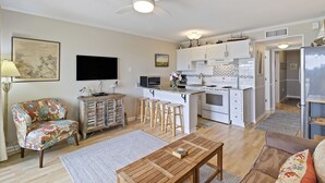 A modern kitchen with white cabinets, a built-in oven, and a microwave. There is a dining area with a wooden table and two bar stools. - Oceanfront Sea Cabin on the Front Beach of Isle of Palms (Isle Of Palms)