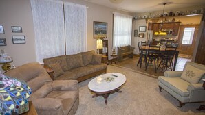 A living room with a sofa, armchair, and coffee table. There is a dining area with a table and chairs.