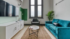 A modern living room with a large window, a teal sofa, a white cabinet, and a small coffee table.