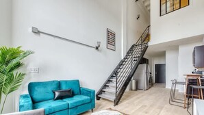 A spacious living area with a teal sofa, a staircase, a kitchen, and a dining area.