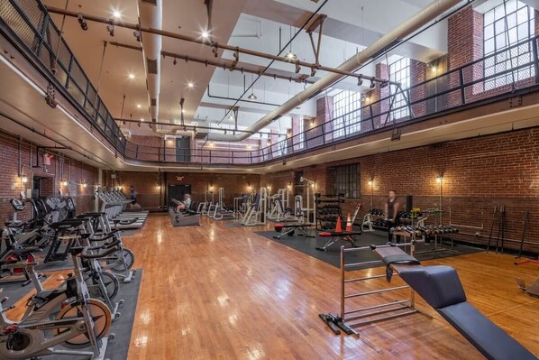 A spacious gym with exercise equipment, wooden floors, and a mezzanine level.