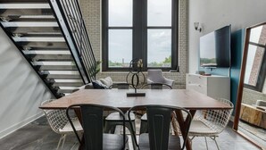 Ett modernt matområde med ett träbord och metallstolar, en trappa och ett stort fönster med utsikt.