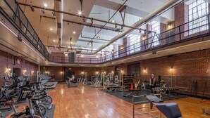 A spacious gym with exercise equipment, wooden floors, and a mezzanine level. - Sosuite | 2BR Loft w W/D, Gym, Lounge (Philadelphia)