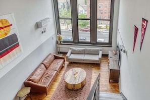 A modern living room with a brown leather sofa, a white sofa, a round coffee table, and a patterned rug. - Sosuite | 2BR Loft w W/D, Gym, Lounge (Philadelphia)