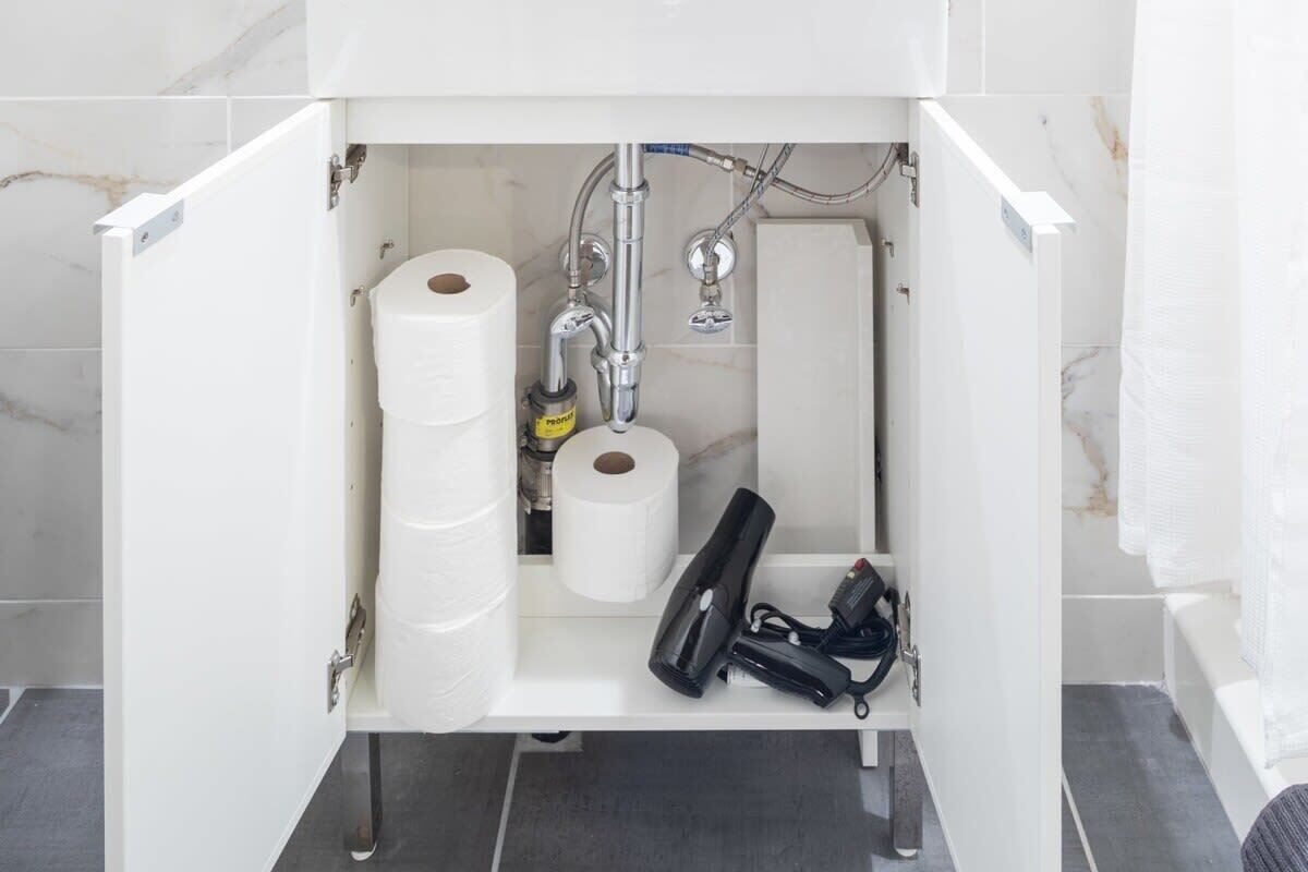 A bathroom cabinet with toilet paper, a hairdryer, and a water heater.