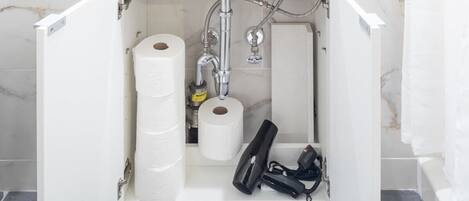 A bathroom cabinet with toilet paper, a hairdryer, and a water heater.