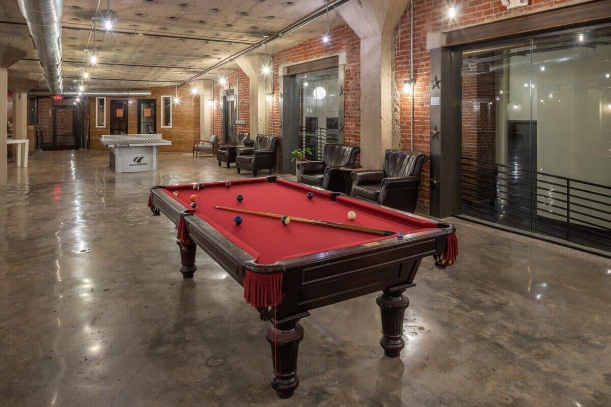 A pool table in a spacious room with brick walls and leather chairs.