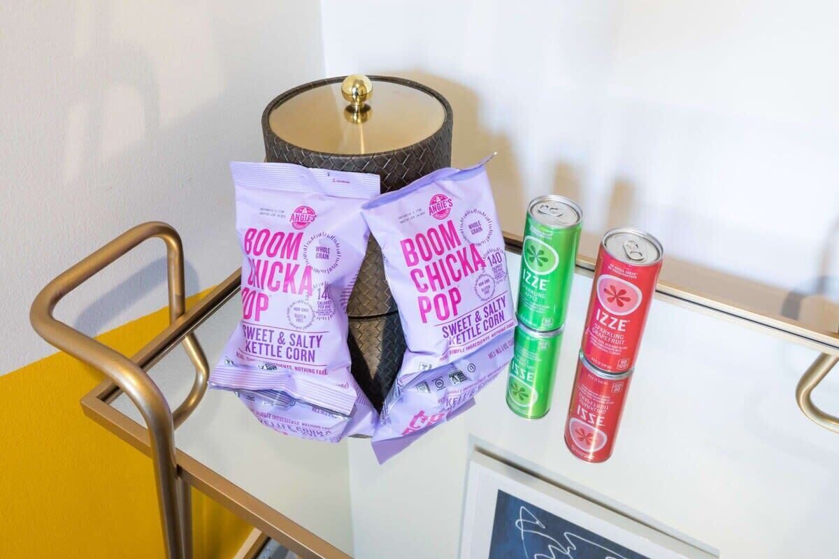 Ett bord med påsar med Boom Chicka Pop-popcorn och Izze-läsk, en lampa och en inramad bild.
