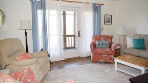 A living room with a beige sofa, a floral armchair, a wooden coffee table, and a patterned rug. - Nature's Retreat- Waterview with Shared Crabbing Pier (Chincoteague)