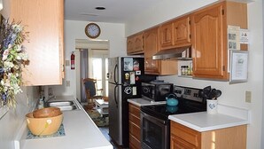 A kitchen with wooden cabinets, a refrigerator, stove, microwave, and a sink. - Nature's Retreat- Waterview with Shared Crabbing Pier (Chincoteague)