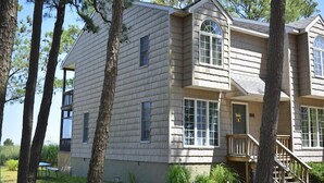 A two-story house with a front porch, large windows, and a staircase leading to the second floor. - Nature's Retreat- Waterview with Shared Crabbing Pier (Chincoteague)