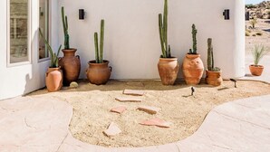 A white building with multiple terracotta pots containing cacti, arranged in a row along the wall. - Casa Blanca by Fieldtrip - Boulder Estate with Hot Tub, Soaking Pool & Outdoor Shower (Yucca Valley)