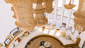 A modern living room with a curved white sofa, a round coffee table, and multiple hanging wicker chandeliers. - Casa Blanca by Fieldtrip - Boulder Estate with Hot Tub, Soaking Pool & Outdoor Shower (Yucca Valley)
