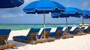 A beach with rows of blue sun loungers and matching umbrellas, a pier in the background, and a clear sky. - Gulf front 2 bedroom with stunning views & Free round of Golf Daily! (Panama City Beach)