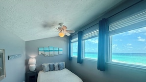 A bedroom with a bed, a ceiling fan, a window with a view of the ocean, and a wall with framed artwork. - Gulf front 2 bedroom with stunning views & Free round of Golf Daily! (Panama City Beach)