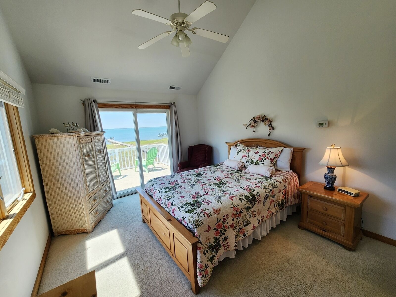 A bedroom with a bed, a nightstand, a dresser, a ceiling fan, and a view of the ocean.