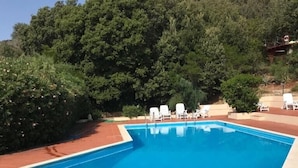 A rectangular swimming pool with a tiled edge, surrounded by white lounge chairs and a backdrop of dense green foliage. - Villa Conca Verde (Conca Verde (SS))