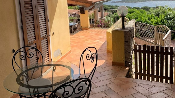 A covered outdoor area with a table and chairs, a view of the sea, and a wooden ceiling. - Villa Conca Verde (Conca Verde (SS))