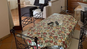 A dining area with a table covered in a fruit-patterned tablecloth, surrounded by metal chairs. - Villa Conca Verde (Conca Verde (SS))