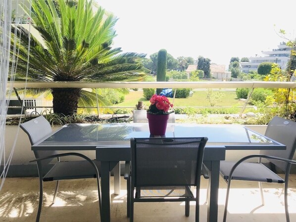 Un balcon avec une table et des chaises en verre, une plante en pot et une vue sur un jardin et des bâtiments.