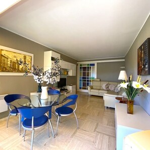 Un salon moderne avec une table à manger en verre, des chaises bleues, un canapé et un téléviseur.