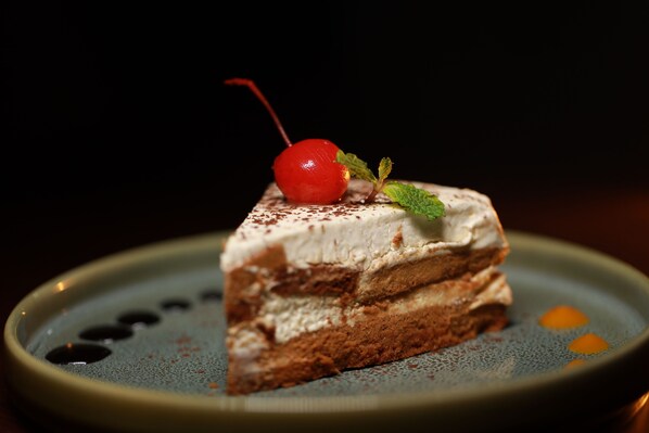 A slice of layered cake with a cherry on top, served on a plate with a dark background.