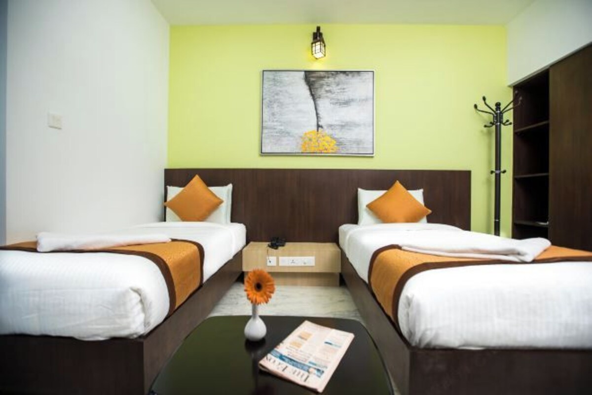Hotelkamer met twee bedden, een nachtkastje, een vaas met een bloem en een kunstwerk aan de muur.
