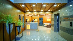 A modern hotel lobby with a reception desk, seating area, and a marble floor.