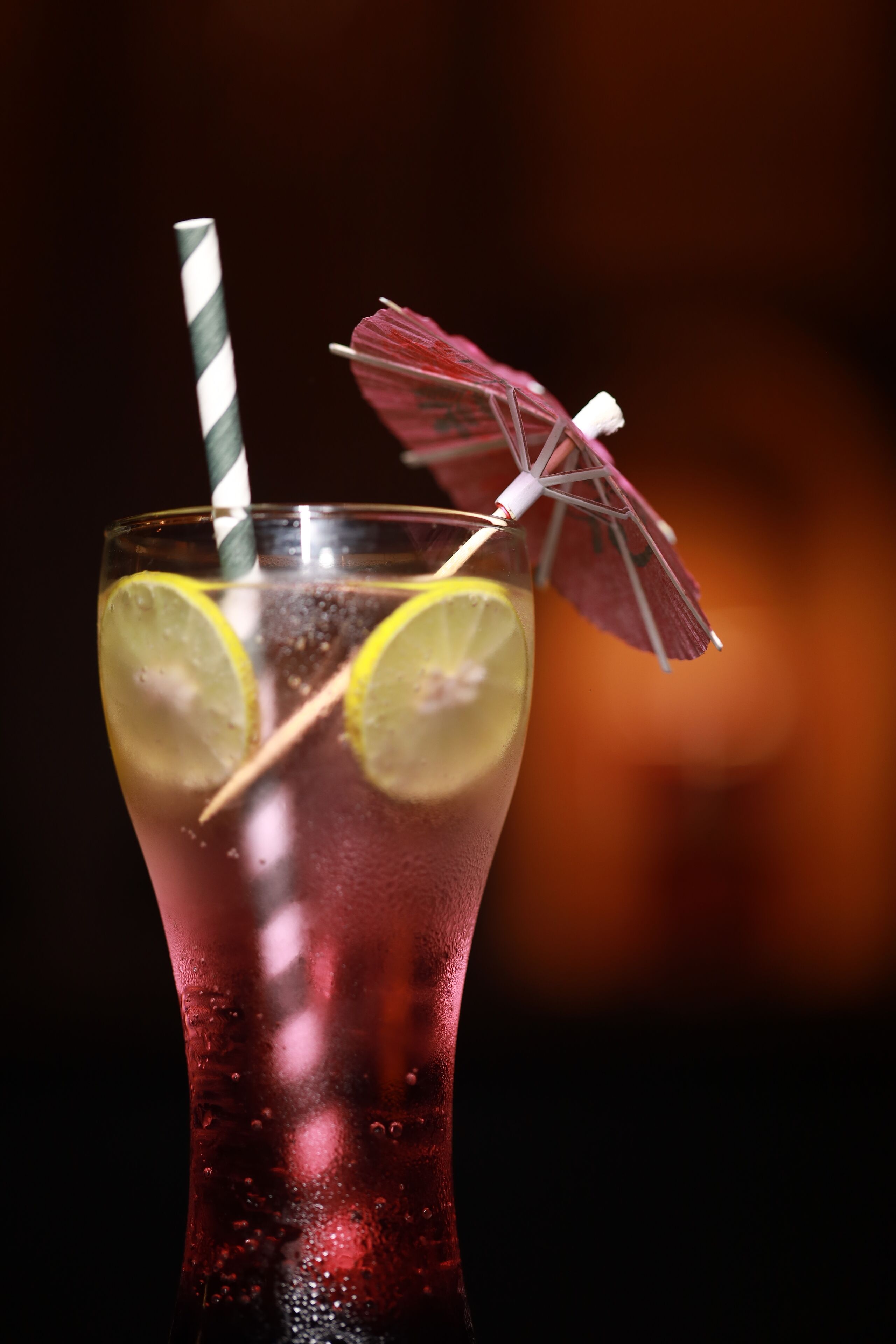 A glass of red beverage with lemon slices and a striped straw.