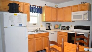 A compact kitchen with wooden cabinets, a white refrigerator, a microwave, a toaster, and a stove.