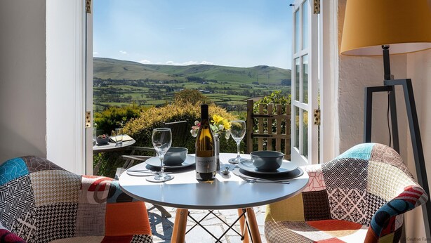 Un coin repas avec une table dressée pour deux personnes, une bouteille de vin et une vue sur des collines ondoyantes.