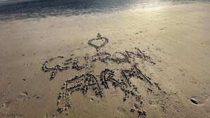 Une plage de sable avec des empreintes et un dessin en forme de cœur.