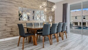 A dining area with a wooden wall, a glass table, and six chairs. - 8 Bedroom Movie Theater In Home Champions Gate! 8 Villa by RedAwning (Davenport)