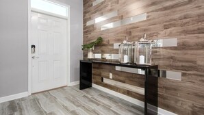 A modern hallway with a white door, a console table with decorative items, and a wall with a wood-like pattern. - 8 Bedroom Movie Theater In Home Champions Gate! 8 Villa by RedAwning (Davenport)