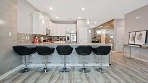 A modern kitchen with a central island, bar stools, stainless steel appliances, and pendant lighting. - 8 Bedroom Movie Theater In Home Champions Gate! 8 Villa by RedAwning (Davenport)