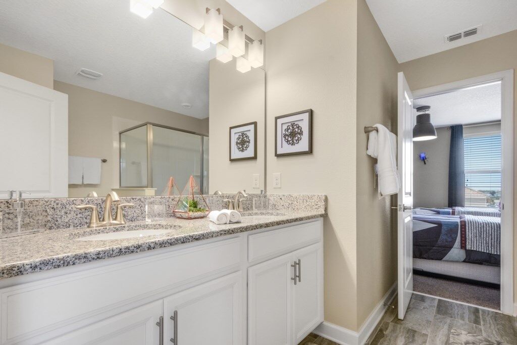 A modern bathroom with a granite countertop, white cabinetry, and a large mirror.