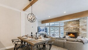 Een gezellig eetgedeelte met een houten tafel voor vier personen, een stenen openhaard en een groot raam met uitzicht op een besneeuwd landschap.