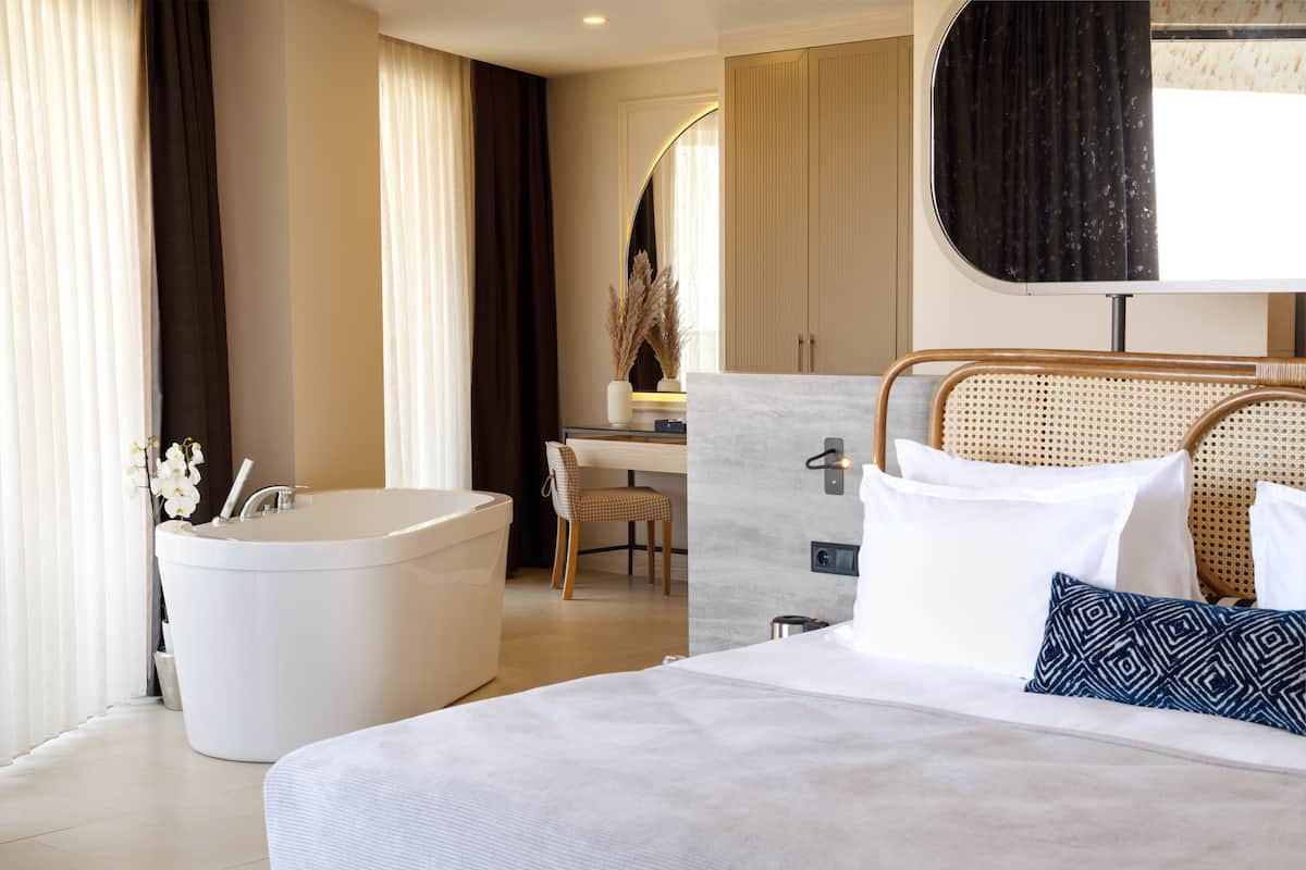 A modern hotel room with a large bed, a separate bathroom with a bathtub, a desk, and a chair.