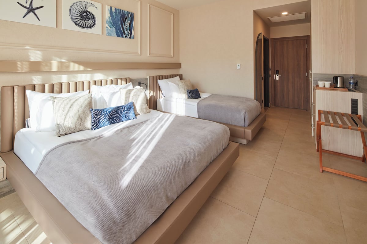 A hotel room with two beds, a kitchenette, and a door leading to another room.