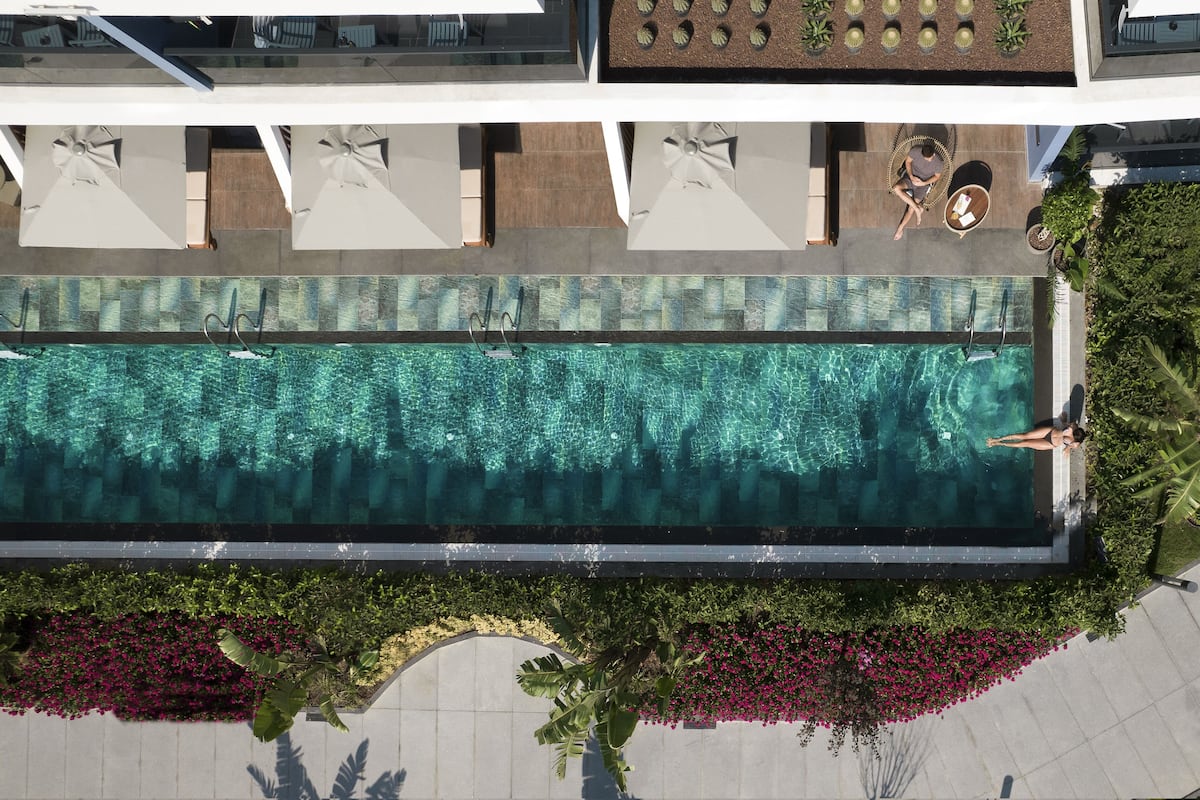 An aerial view of a modern hotel pool area with a clear pool, lounge chairs, and a small seating area.