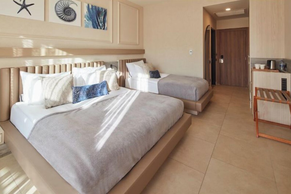 A hotel room with two beds, a wooden bench, and a kitchenette.