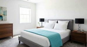 Un dormitorio con cama, mesitas de noche, cómoda, ventana y un cuadro.