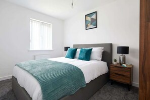 A bedroom with a bed, bedside tables, a window, and a wall-mounted picture.