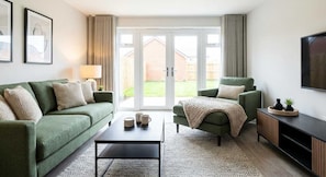 Una sala de estar con un sofá verde, un sillón verde, una mesa de centro y un televisor sobre un mueble de madera.