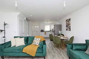 Una sala de estar moderna con un sofá verde, una manta amarilla y un comedor con sillas verdes.