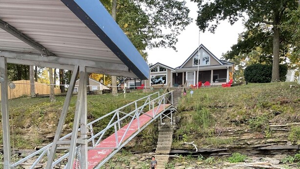 Un puente que conduce a un muelle sobre aguas tranquilas, con una casa al fondo.