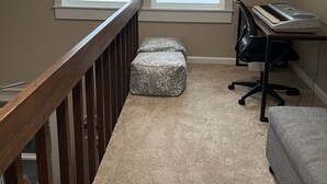 Una habitación con vistas a un lago a través de un ventanal grande, una barandilla de madera, un escritorio con teclado y un banco acolchado.