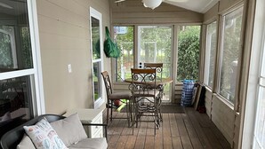 Un solarium con terraza de madera, un sofá, una mesa de comedor con sillas y un ventilador de techo.